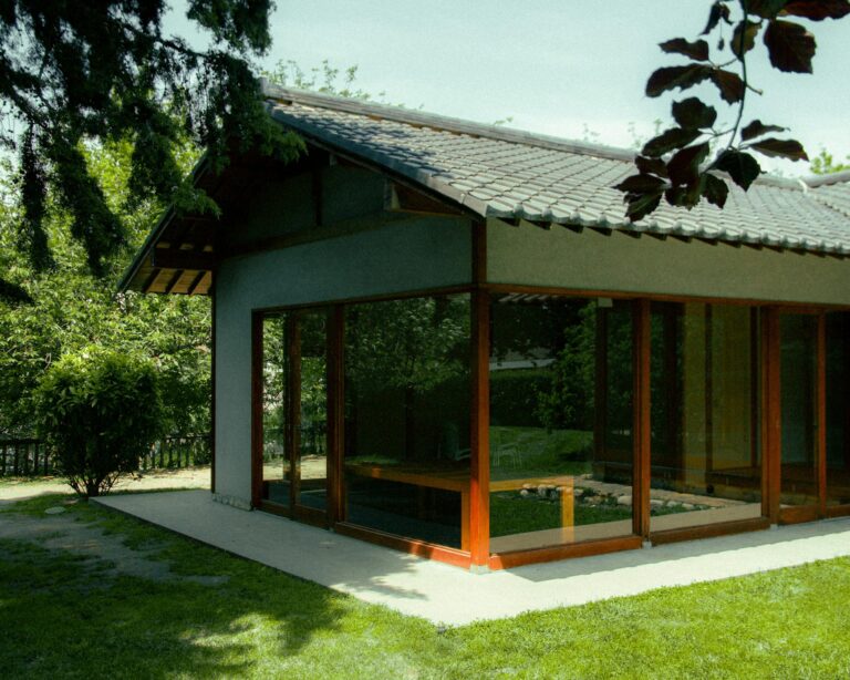 Contemporary bungalow featuring glass windows amid lush greenery. Ideal for serene living.