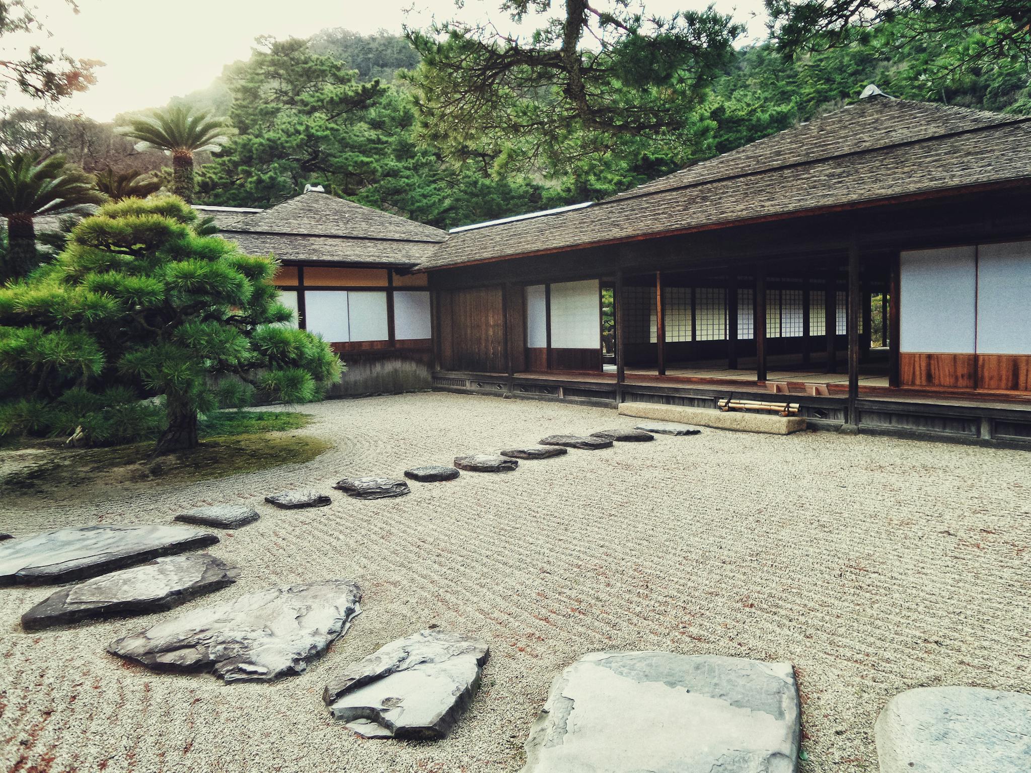 Serene Japanese Zen garden with stone path, lush greenery, and traditional wooden architecture.
